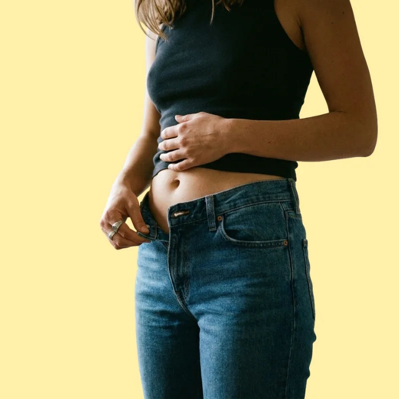 Woman tugging at her jeans waistband, midsection looking puffy and tight