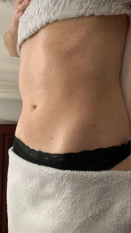 A close-up of a person's midsection wearing a black lace-trimmed underwear bottom and a white towel wrapped around the lower body.